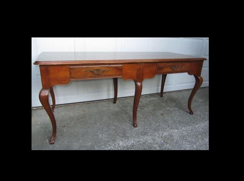 May include: A long, rectangular wooden table with three drawers and cabriole legs. The table is made of a dark wood with a natural finish.