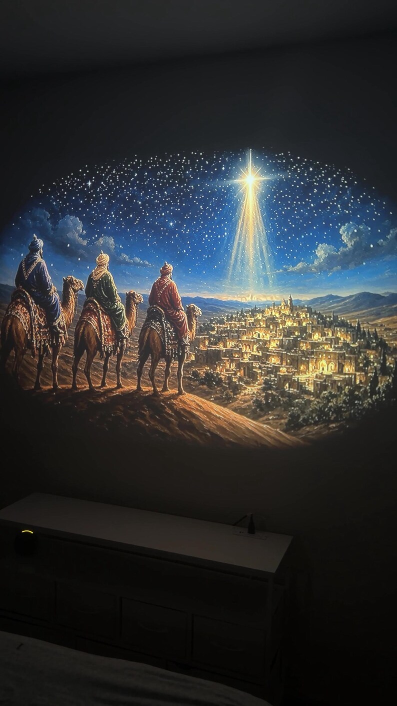 May include: A wall projection displaying a scene of three figures riding camels across a desert landscape towards a glowing city under a night sky. A bright, radiant star shines above the city, casting light over the illuminated buildings.