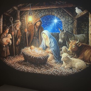 May include: A projection of a nativity scene featuring a central infant in a manger, a woman in a blue head covering, a man with a staff, a child holding a lamb, a donkey, a cow, and sheep. A glowing lantern hangs above, and a bright star shines in the background.