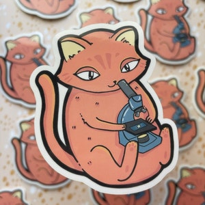 May include: A sticker featuring an orange cat with yellow ears and a white outline, holding a blue microscope. The cat has a relaxed expression. Multiple stickers are visible in the background.