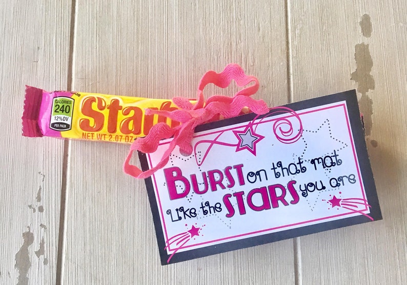 May include: A black card with white text that reads "BURST on that mat Like the STARS you are" with a pink ribbon and a yellow candy bar.