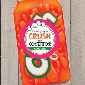 K&ouml;nnte beinhalten: Orangefarbene Limonade-Dose mit einem rosa runden Aufkleber, auf dem steht "You are going to CRUSH the COMPETITION! GOOD LUCK!"