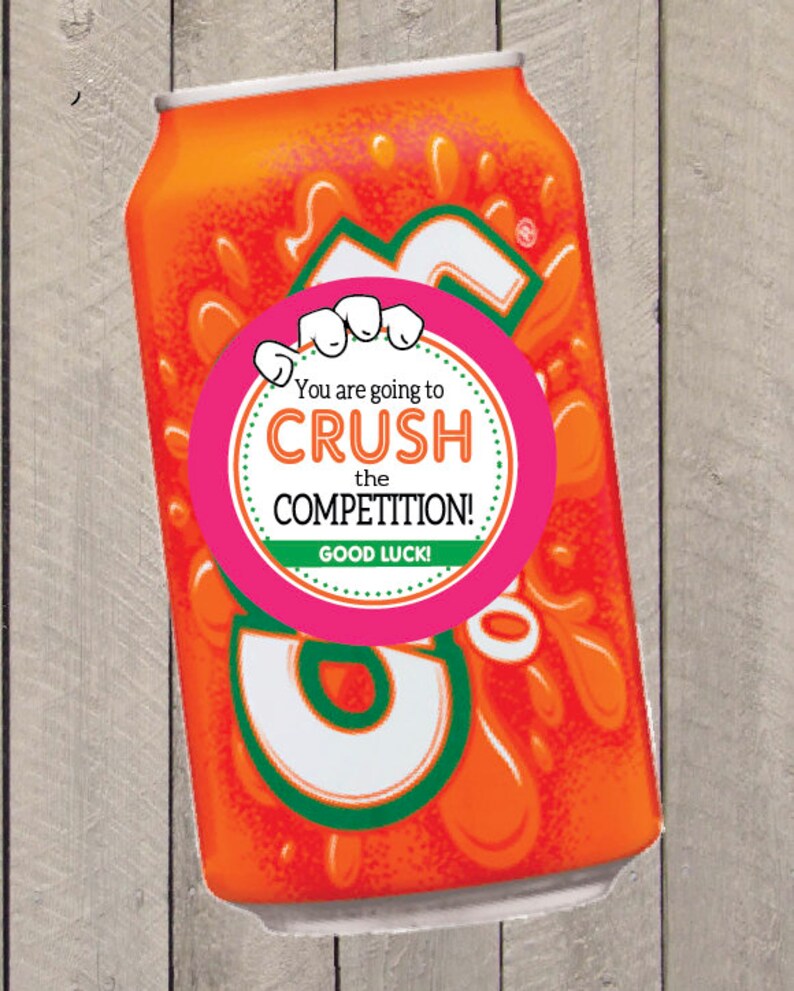 K&ouml;nnte beinhalten: Orangefarbene Limonade-Dose mit einem rosa runden Aufkleber, auf dem steht "You are going to CRUSH the COMPETITION! GOOD LUCK!"