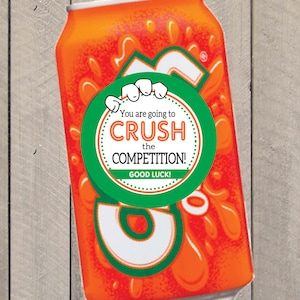 K&ouml;nnte beinhalten: Eine orangefarbene und gr&uuml;ne Dose mit einem wei&szlig;en runden Aufkleber, auf dem steht "You are going to CRUSH the COMPETITION! GOOD LUCK!"