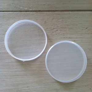 May include: Two clear plastic lids for containers. The lids are round and have a smooth surface.