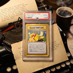 以下が含まれることがあります： 透明な保護ケースに入った1998年P.M. Japanese Promoピカチュウイラストレーターのトレーディングカード。カードには筆を持った黄色いピカチュウが描かれており、表面には「ILLUSTRATOR」の文字と日本語のテキストが印刷されています。