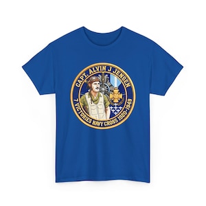 May include: A royal blue short-sleeve t-shirt featuring a circular graphic on the chest. The design depicts a pilot in flight gear, a propeller, and a medal, with the text CAPT. ALVIN J JENSEN, 7 VICTORIES NAVY CROSS 1920-1949 in gold lettering.