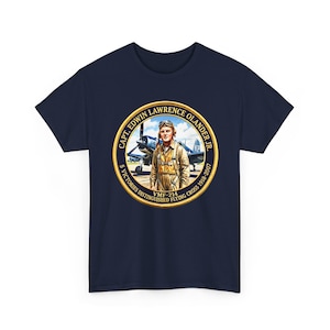 Może przedstawiać: Granatowy t-shirt z okrągłą grafiką przedstawiającą portret kapitana Edwina Lawrence'a Olandera Jr. w stroju lotniczym, samolot myśliwski w tle oraz napis Capt. Edwin Lawrence Olander Jr. 5 Victories Distinguished Flying Cross 1918-2007 VMF-214.