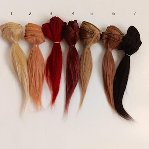 Peut inclure: Sept paquets d'extensions de cheveux de différentes couleurs sont présentés sur un fond blanc. Les couleurs vont du blond clair au brun foncé et au noir. Chaque paquet est attaché avec un petit élastique.