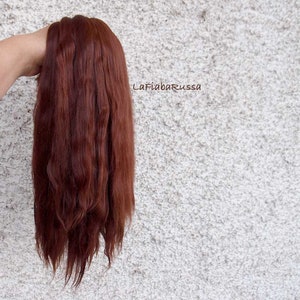 May include: A long, straight, auburn-colored hair extension. The hair is held in a hand, with the ends of the hair extending down.