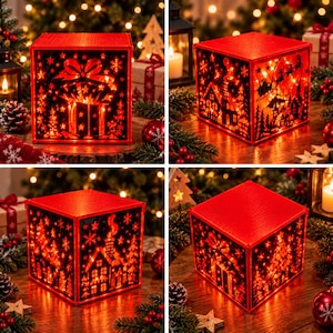 Peut inclure: Une boîte lumineuse cubique rouge présentant des silhouettes noires découpées complexes de scènes de Noël, incluant un cadeau avec un nœud, une maison avec une cheminée et un traîneau avec des rennes, éclairée par des lumières chaudes.