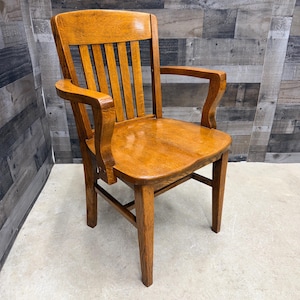 May include: A wooden armchair with a warm, honey-toned finish. The chair features a slatted backrest, curved armrests, and a contoured seat. The legs are sturdy and angled, providing stability. The chair is designed for comfort and support.