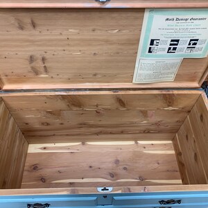 Pu&ograve; includere: Un baule in cedro blu chiaro con interno in legno. Il baule &egrave; aperto e il coperchio &egrave; sollevato. Un certificato di garanzia contro le tarme &egrave; visibile all'interno del baule.