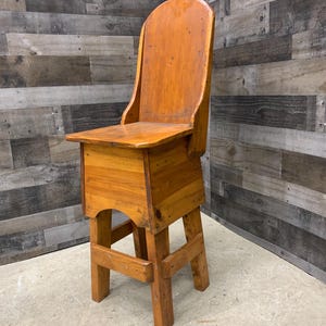 May include: A wooden chair with a high back and a seat that is raised on a set of four legs. The chair is made of natural wood and has a rustic appearance.