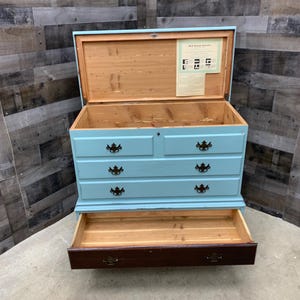 Pu&ograve; includere: Un baule di legno blu chiaro con quattro cassetti e un coperchio a ribalta. Il baule &egrave; aperto, rivelando un interno rivestito in cedro. Il baule ha un'etichetta all'interno del coperchio che recita "Mail Boxes Etc. Furniture".