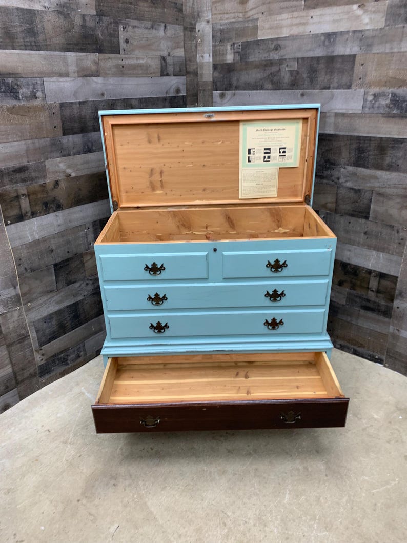Pu&ograve; includere: Un baule di legno blu chiaro con quattro cassetti e un coperchio a ribalta. Il baule &egrave; aperto, rivelando un interno rivestito in cedro. Il baule ha un'etichetta all'interno del coperchio che recita "Mail Boxes Etc. Furniture".