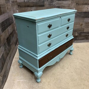 Pu&ograve; includere: Un antico baule dipinto di azzurro con quattro cassetti e un coperchio superiore. Il baule ha un fondo in legno scuro e piedini decorativi.