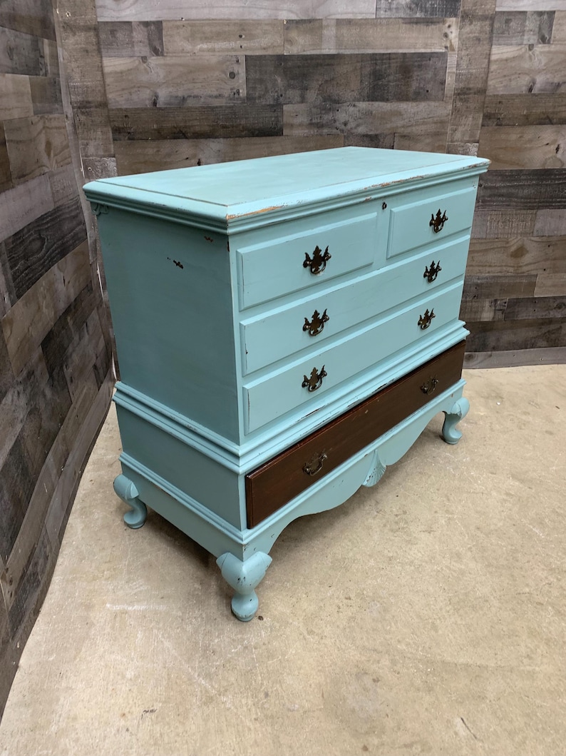 Pu&ograve; includere: Un antico baule dipinto di azzurro con quattro cassetti e un coperchio superiore. Il baule ha un fondo in legno scuro e piedini decorativi.