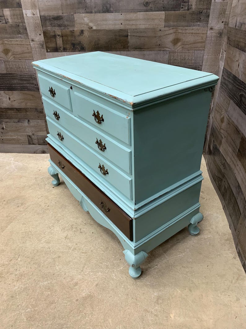 Pu&ograve; includere: Un antico baule di colore azzurro chiaro con quattro cassetti e un coperchio superiore. Il baule ha una base in legno scuro e piedini decorativi.