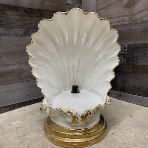 May include: A white ceramic seashell lamp with gold accents. The lamp has a pearlescent finish and a single light bulb in the center.