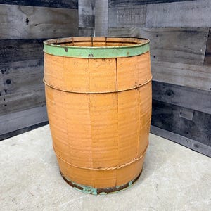 May include: An orange wooden barrel with green metal bands around the top and bottom. The barrel has a rustic, weathered appearance, suggesting it is vintage or antique. The barrel is cylindrical and stands upright.