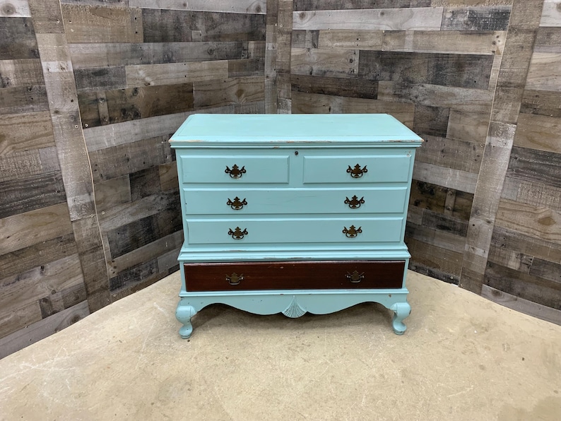 Pu&ograve; includere: Un baule in legno dipinto di azzurro con quattro cassetti e un cassetto inferiore. Il baule ha gambe ornate e ferramenta in ottone.