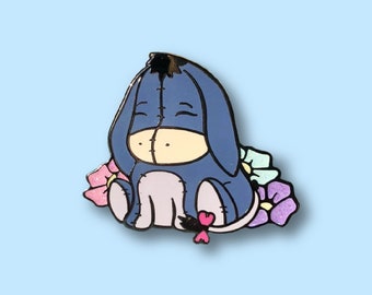 May include: A blue and purple enamel pin featuring a cartoon donkey with a pink heart and surrounded by colorful flowers.