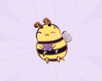 May include: A yellow and black enamel pin of a cartoon bee holding a purple flower. The bee has a smiling face and a pair of wings.
