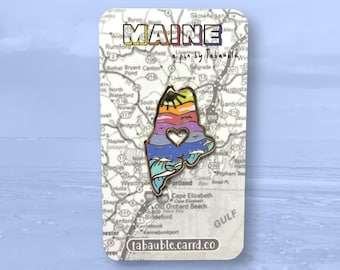 May include: A gold enamel pin shaped like the state of Maine with a rainbow heart and a sun with a smiling face. The pin is on a white background with a map of Maine.