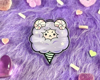 May include: A whimsical pin featuring a cartoon cotton candy character with a grumpy expression. The pin is lavender with white accents and a green cone. The image is surrounded by colorful candies on a purple, fluffy surface.