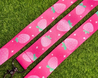 May include: Pink lanyard with a white and green strawberry pattern. The lanyard has a silver metal hook.