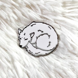 May include: A white enamel pin of a curled up sleeping wolf. The pin is silver and has a shiny finish.