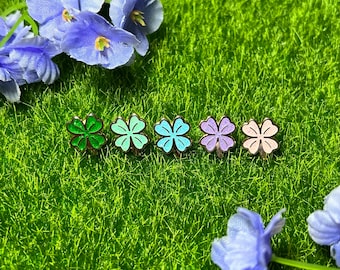 May include: Five gold-colored four-leaf clover charms with different colored enamel. The charms are green, light green, blue, purple, and pink.