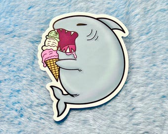 May include: A blue cartoon shark with an open mouth eating a three-scoop ice cream cone. The ice cream is pink, green, and white.