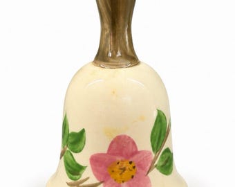 May include: A ceramic bell with a cream-colored body and a glossy brown handle. The bell features a hand-painted design of a single pink flower with a yellow center and green leaves on a brown stem, centered on the front of the bell's body.