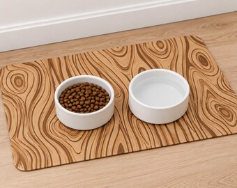 May include: A rectangular pet feeding mat with a brown and tan wood grain pattern featuring two white ceramic bowls, one filled with brown dry kibble and the other filled with clear water, placed side by side on the surface.