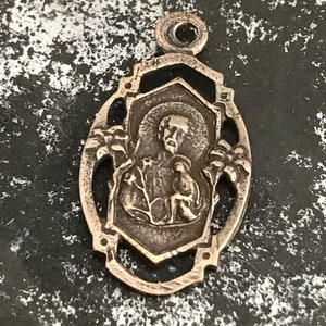 May include: Silver pendant with an ornate design featuring a religious figure in the center.