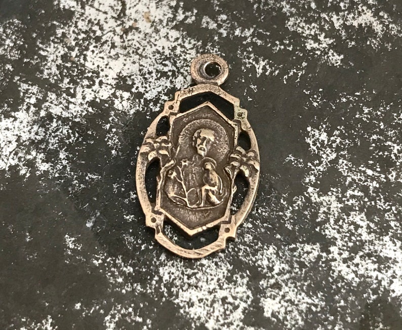 May include: Silver pendant with an ornate design featuring a religious figure in the center.