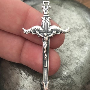 May include: A silver pendant in the shape of a crucifix with a detailed design. The crucifix features a figure of Jesus Christ on the cross.