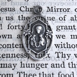 May include: Silver charm pendant featuring a religious image of a woman holding a baby. The charm is in a detailed, ornate style.