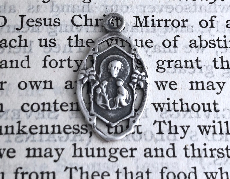 May include: Silver charm pendant featuring a religious image of a woman holding a baby. The charm is in a detailed, ornate style.
