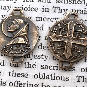 May include: Two antique bronze medallions with a connector. The first medallion features a profile of a man with the text "IN CALCE DRAGIN" around the edge. The second medallion features a cross with the letters "B.C.S.P.M.D.S" around the edge.