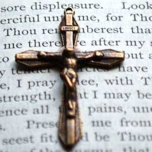 May include: A bronze crucifix with a figure of Jesus Christ on the cross. The crucifix is resting on a page of a book with text.