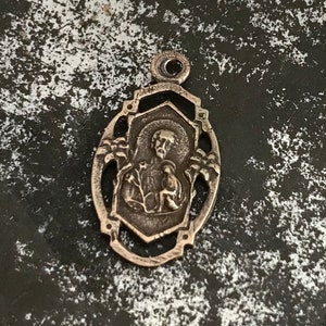 May include: Silver pendant featuring a detailed image of a religious figure with a halo, surrounded by an ornate design.