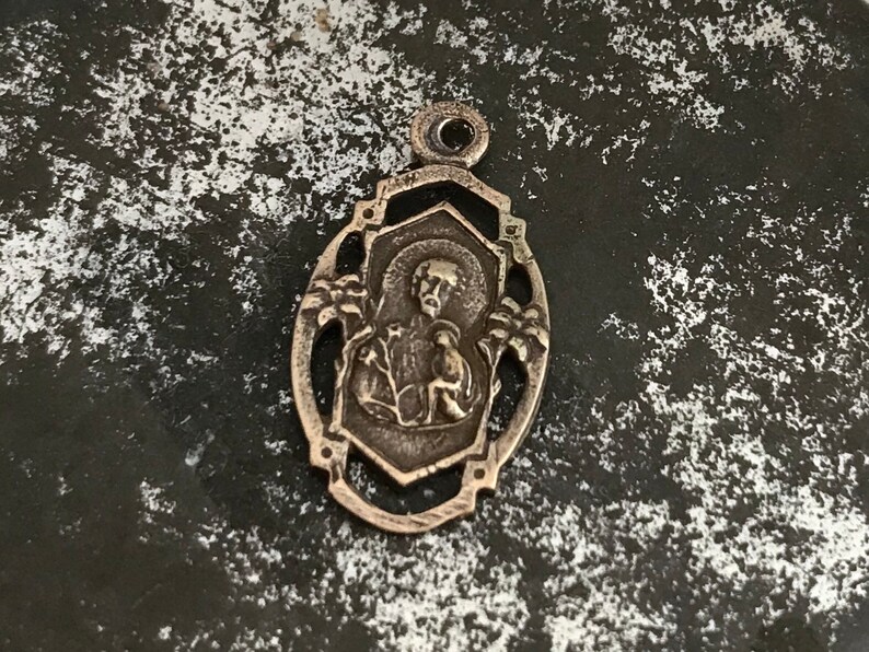 May include: Silver pendant featuring a detailed image of a religious figure with a halo, surrounded by an ornate design.