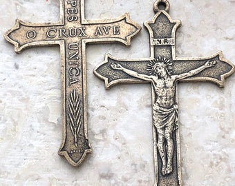 May include: Two antique bronze crosses. The larger cross features a depiction of Jesus Christ on the cross. The smaller cross has the inscription "O CRUX AVE SPES UNICA".