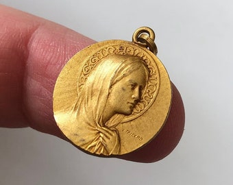 May include: Gold-toned metal pendant featuring a profile of the Virgin Mary with a halo. The pendant is inscribed with "TRICANO".