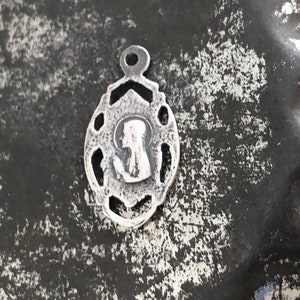 May include: A silver charm with a detailed design featuring a silhouette of a woman's head. The charm has a loop at the top for attaching to a necklace or bracelet.