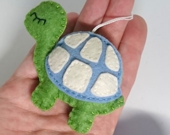 May include: A small felt turtle ornament with a blue shell and green body. The shell has white circles sewn on it. The turtle has a white eye with a black eyelash.