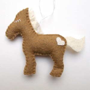 May include: A brown felt horse ornament with a white felt mane and tail. The horse has a white felt heart on its side.